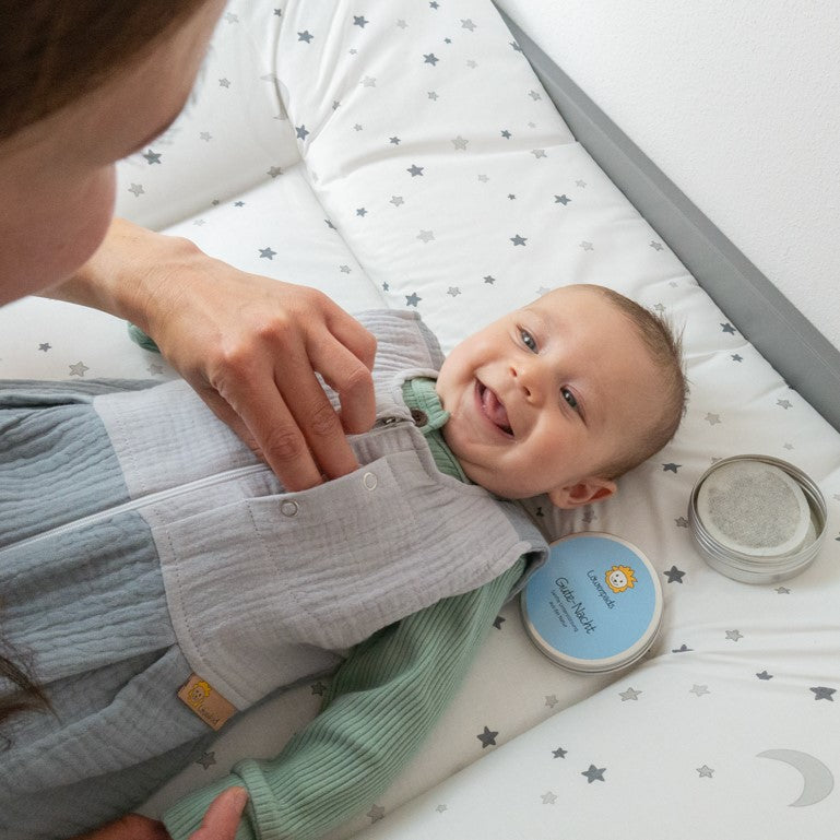 Baby auf Wickeltisch mit Loewenkind Schlafsack und Gute-Nacht Kraeuterpad-Dose